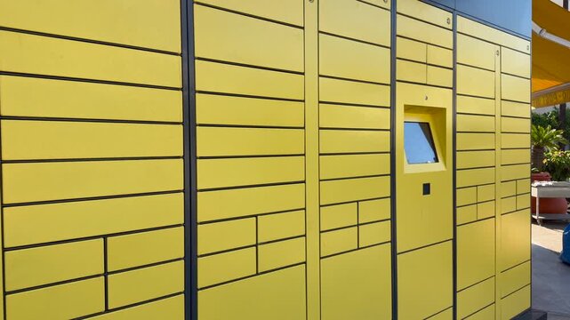 Yellow parcel lockers form automated delivery system with integrated touchscreen kiosk. Locker bank offers convenient logistics solution for customer parcel pickup. Efficient and contactless logistics