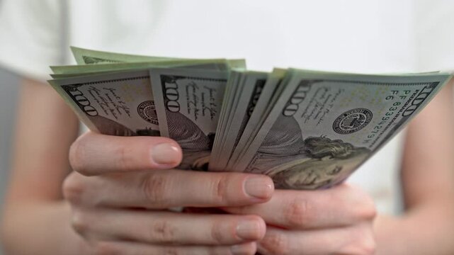 Woman in white t-shirt counting stack of dollar banknotes. Personal finance, cash savings, income, wealth, investment, budgeting and money management concept.	
