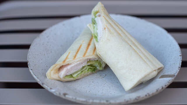 Two grilled chicken wraps with lettuce on a speckled plate. The background is blurred,