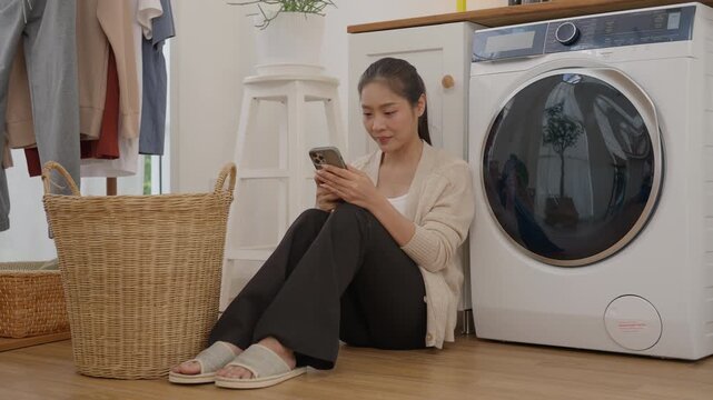 Woman Using Smartphone Beside Washing Machine and Laundry Basket Cleaning Clothing at Home, Calm Domestic Routine with Modern Appliance, Bright Interior, Everyday Washing and Household Comfort