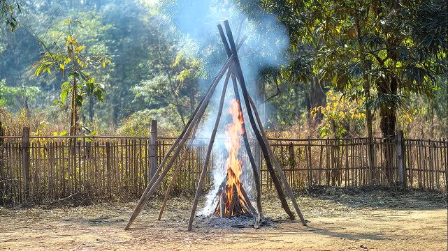 Small rural ceremonial fire burning beneath a wooden tripod frame, smoke rising through surrounding trees, traditional heritage ritual, outdoor spiritual ceremony, sacred flames, cultural customs