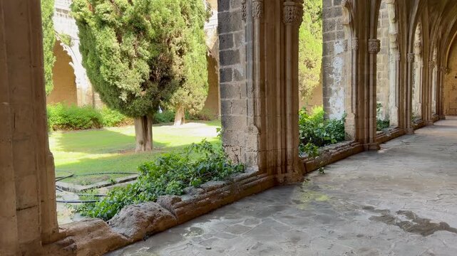 Kyrenia, Cyprus - October 3, 2026 Bellapais Abbey cloister extends beneath carved Gothic arches beside quiet garden. Abbaye de la Paix reveals sunlit stone walkway and historic monastic architecture.
