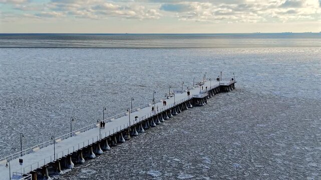 Aerial drone shot of the Orłowo pier reaching out over the frozen Baltic Sea covered with drifting ice on a sunny winter day, Gdynia, Poland