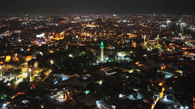 High angle drone perspective reveals glowing architectural landmarks, roads, and residential sprawl during evening.