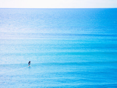 Distant paddleboarder in vast blue sea