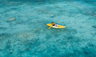 Aerial view of a woman relaxing on a yellow kayak over a beautiful coral reef in crystal clear turquoise sea water. © SASITHORN