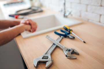 Obraz na płótnie Canvas Big and small wrenches on table in kitchen. Screwdriver and nippers. Man's hands on sink. Daylight.