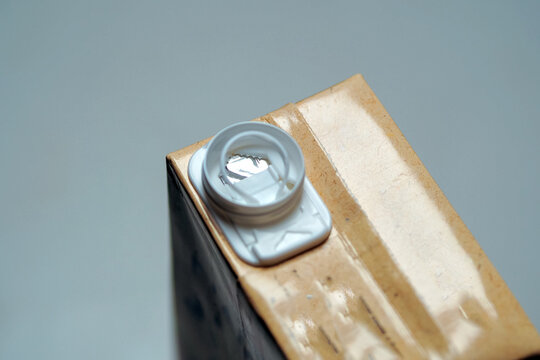 close-up view of a beverage carton top showing a white plastic spout with an inner pull-ring seal on a beige paper packaging.
