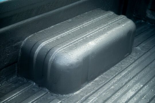 Close up of wet truck bed liner surface with raindrops after a storm.
A high-quality close-up photograph capturing the textured black or dark grey truck bed liner interior of a pickup truck