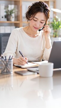 ヘッドセットを使いノートにメモする女性と手前の余白の縦構図