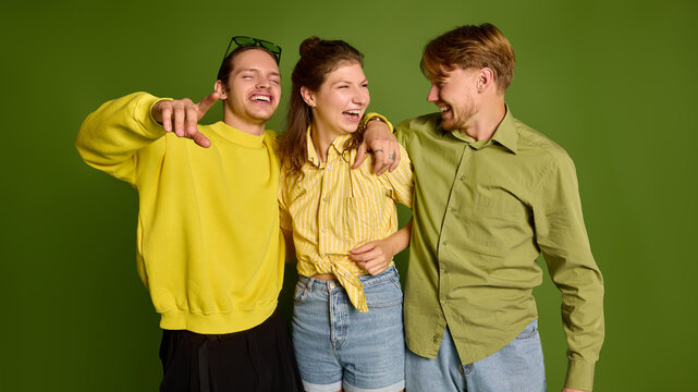 Smiling young companions embracing shoulders against green studio backdrop with warm affection. Social belonging, friendship support, emotional connection concept.