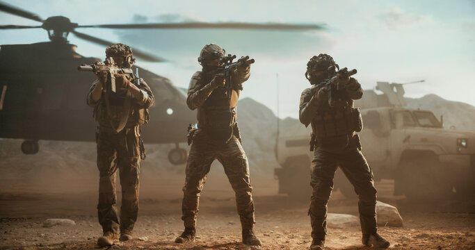 Three-man Infantry Fire Team in Full Tactical Gear Holds a Defensive Line With Raised Assault Rifles, Covering a Dusty Desert Landing Zone Where a Transport Helicopter and Armored Vehicle Wait.