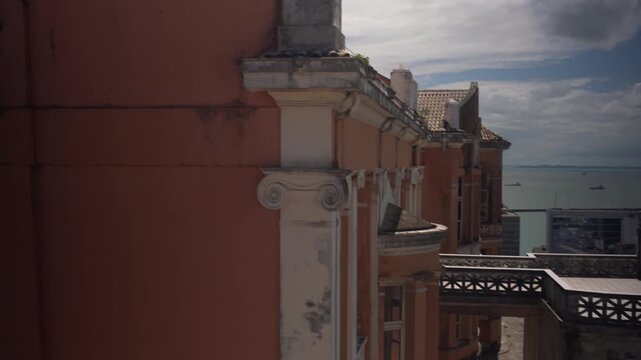 The camera moves across the rooftops of a historic pink building in Pelourinho with views of the Bay of All Saints, ending on a smiling woman, Salvador, Brazil