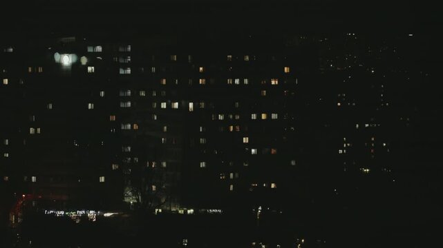 Lights in the windows of a large multi-story apartment building turning on and off during the night, revealing the rhythm of urban life and the patterns of electricity consumption. timelapse