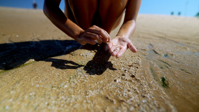 Woman examining wet sand in her palm at the shoreline