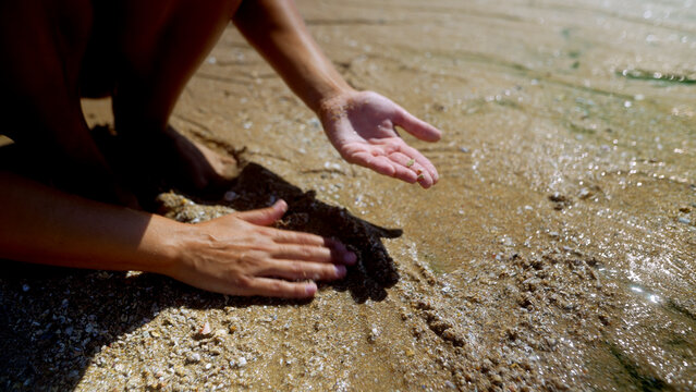 Woman touching wet sand beside shallow seawater