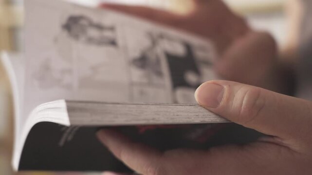 Person reading manga comic next to a library of books