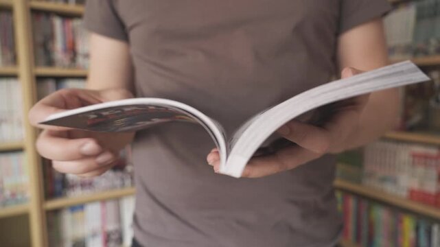 Person reading manga comic next to a library of books