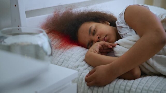 Child sleeps peacefully on bed. Soft lighting highlights calm expression. Red streaks appear in hair, adding visual contrast. Scene suggests innocence disrupted by mystery. Use for stories, films
