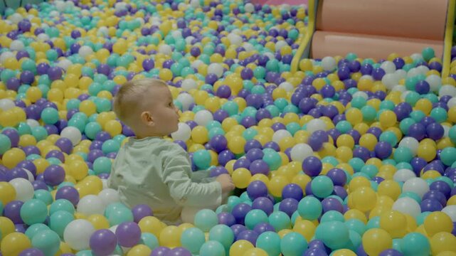A little boy sits and plays in a ball pit filled with colorful plastic balls. He enjoys the vibrant setting in an indoor play area.