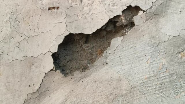 Damaged plaster wall with cracks and peeling paint. Close-up of a severely damaged, aged plaster wall. Heavy cracks and large areas of peeling and spalling paint layers are prominent across.
