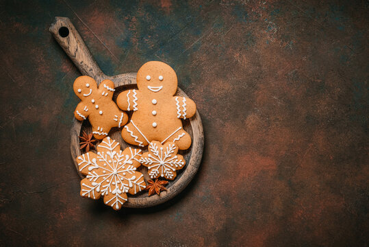 Gingerbread men and snowflakes in a wooden plate on a dark rustic background, top view, flat lay, copy space