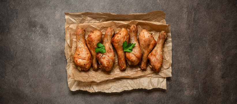 Roasted chicken drumsticks on paper, dark rustic background,close-up, top view, flat lay, copy space, banner