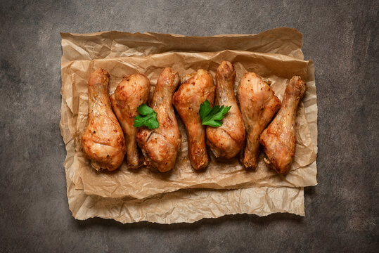 Roasted chicken drumsticks on paper, dark rustic background,close-up, top view, flat lay, copy space