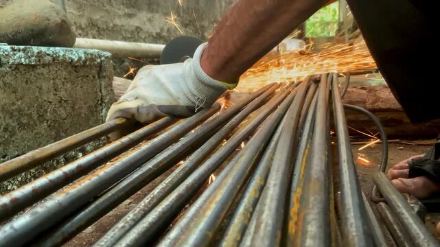 A construction worker using an angle grinder to cut steel rebar on a building site, with visible sparks flying during the metalworking process.