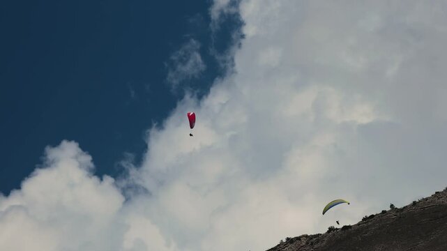 paragliders soaring high above scenic mountain cliffs and white clouds under a deep blue sky.