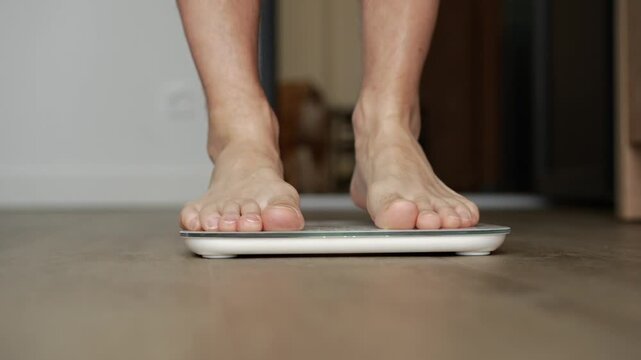 A man checks his weight by stepping onto an electronic scale.
A man stands on the scale to find out his weight.