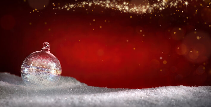 Shiny glass bauble on snow and magical red sparkling Christmas background with copy space