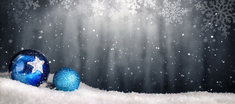 Two shiny blue baubles on snow and magical snowy gray Christmas background with nicely illuminated copy space