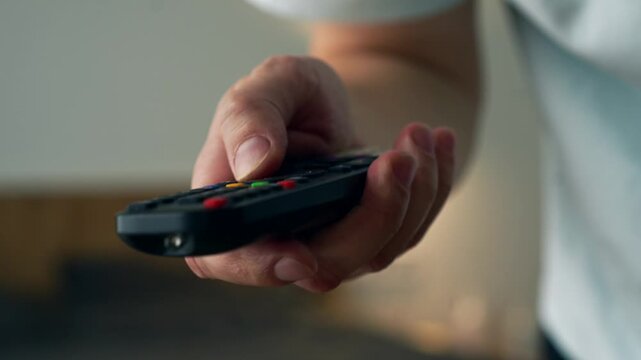 Frustrated Young Man Trying to Change TV Channels with a Malfunctioning Remote Control