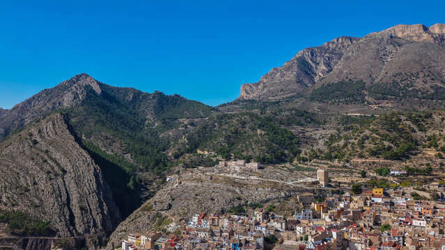 Aerial view of the historic town of Xixona with its castle ruins, dense urban area with terracotta rooftops, and rugged mountain landscape in Xixona, Valencian Community, Spain.