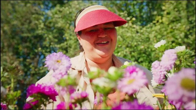 Woman smiles among vibrant purple and pink flowers. Sunlit garden scene, bright and cheerful. Perfect for spring, gardening, or nature projects. Flowers are daisies and asters