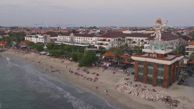 Kuta beach in Bali Indonesia busy with tourists on the sand ocean waves hotels and palm trees along the shore a crowded tropical beachfront holiday travel destination aerial drone view