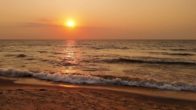 Waves break onto a sandy Lake Malawi beach in slow motion as the setting sun casts warm golden reflections across the water.
