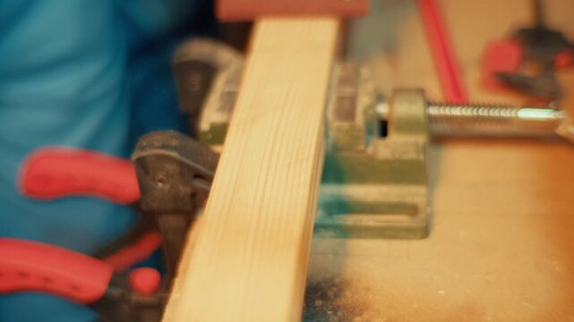 Slow motion close-up of hands using a red sanding block to smooth a wooden plank clamped in a vise. Authentic DIY woodworking footage for craft, carpentry and maker projects