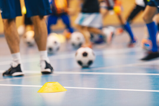 Indoor Futsal Training Session Showing Players Legs and Soccer Balls Around Yellow Marker Cone on Gymnasium Floor