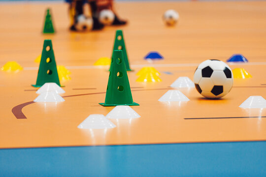 Indoor Futsal Training Setup with Green Cones, White Marker Domes, and Soccer Ball on Gymnasium Floor