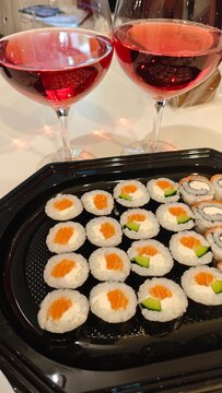 Sushi rolls with salmon and avocado beside two glasses of red wine on a table, close up of a prepared meal and drinks
