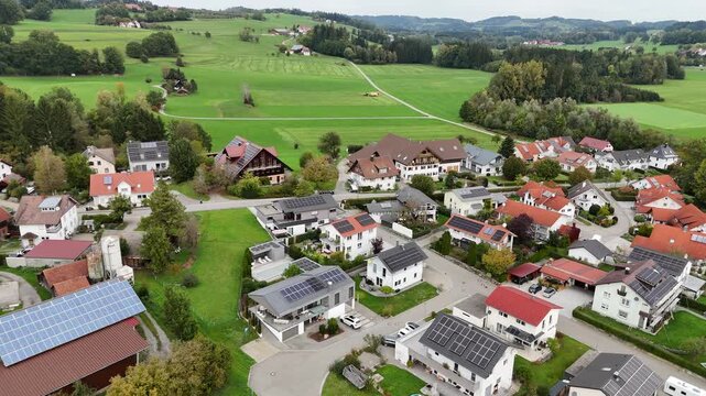 Aerial view of German village with houses, green fields and tractor harvesting grass fodder