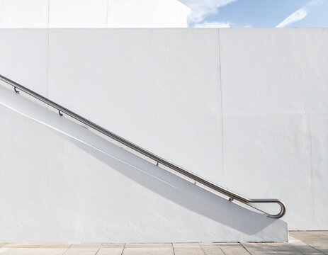 Stainless steel handrail along a sloping ramp on a white wall with large blank space above