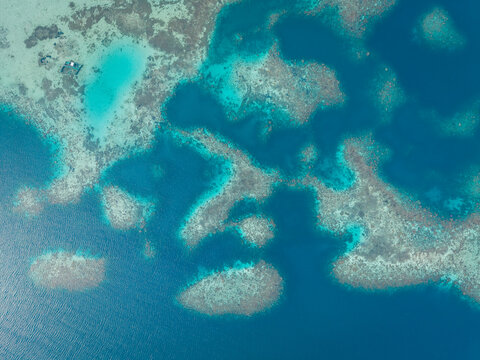 Aerial view of a vibrant coral reef surrounded by crystal clear turquoise and deep blue ocean waters in Karimunjawa, Central Java, Indonesia.