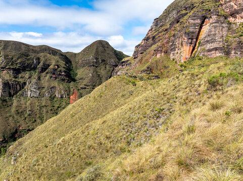 Aerial view of the Codo de los Andes featuring rugged rocky cliffs, steep grassy slopes, and mountain ridges under a blue sky in Samaipata, Santa Cruz Department, Bolivia.