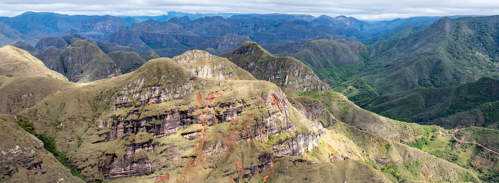 Aerial view of Codo de los Andes with rugged sandstone rock formations, steep cliffs, and rolling green hills under a cloudy sky in Samaipata, Santa Cruz Department, Bolivia.