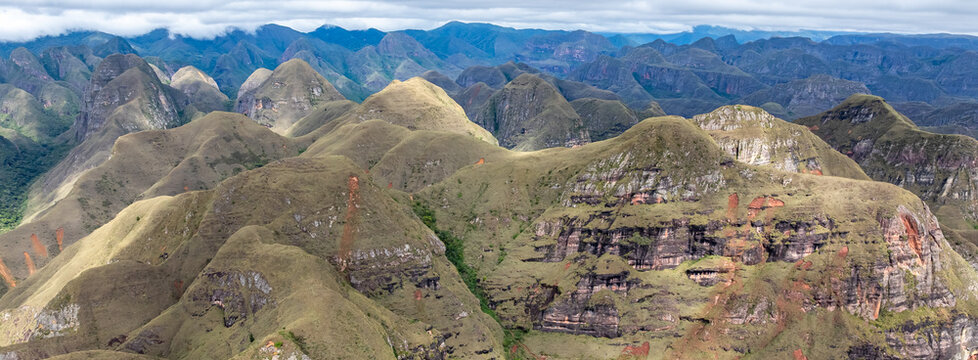 Aerial view of Codo de los Andes featuring rugged mountain ridges, rocky cliffs, and rolling grassy hills under a cloudy sky in Samaipata, Santa Cruz Department, Bolivia.