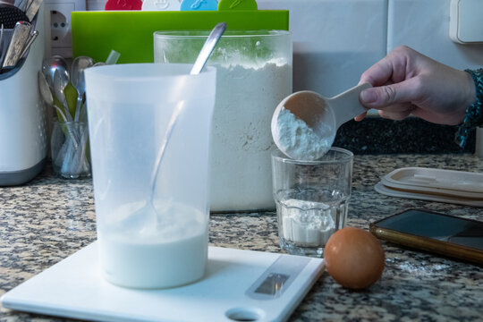 Woman hand adding cornstarch or flour with scoop while baking in kitchen.