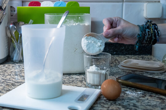 Woman hand adding cornstarch or flour with scoop while baking in kitchen.